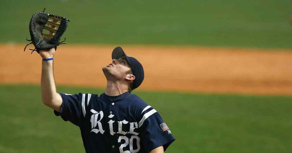 A baseball player in a blue jersey with 'Rice' printed raises his glove triumphantly on a baseball field with a dirt infield, representing the dedication and skill often associated with discussions around a bullpen catcher salary.
